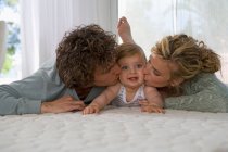 Laying parents kissing baby — Stock Photo