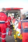 Los paramédicos levantando a la mujer en camilla en ambulancia - foto de stock