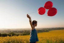 Girl carrying balloons in field — Stock Photo