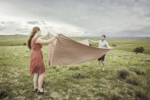 Young couple on hilltop folding pink blanket, Cody, Wyoming, USA — Stock Photo