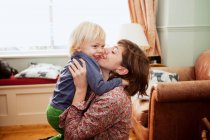 Mãe segurando e beijando filho na sala de estar — Fotografia de Stock