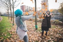Two young women play fighting with autumn leaves in park — Stock Photo