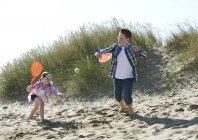 Chica y niño jugando con naranja bate deportivo y pelota de tenis en las dunas - foto de stock