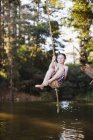 Jeune garçon utilisant corde balançoire sur le lac — Photo de stock