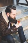 Молодой бородатый мужчина курит трубку на ступеньках — стоковое фото