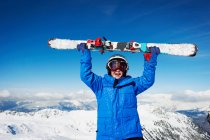Niño sosteniendo esquís en la cima de la montaña nevada - foto de stock