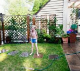 Menino brincando no aspersor no quintal — Fotografia de Stock