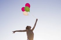 Low angle view of mature woman holding up bunch of balloons against blues sky — Stock Photo