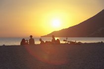 Silhouettes de petits groupes de personnes regardant le coucher du soleil sur la plage, Vigan, Croatie — Photo de stock