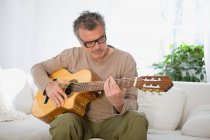 Homem dedilhando guitarra em casa — Fotografia de Stock