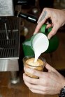 Mani di cameriere caffè versando schiuma di latte in vetro latte — Foto stock