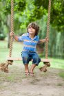 Усміхнений хлопчик сидить у гойдалці на дереві — стокове фото