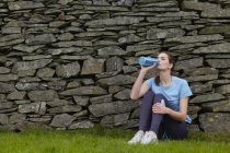 Runner drinking water against rock wall — Stock Photo