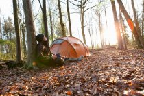 Man drinking coffee by tent in forest — Stock Photo