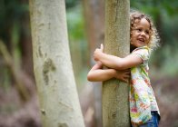 Young girl hugging tree smiling — Stock Photo