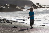 Мальчик ходит волнами по пляжу — стоковое фото