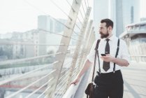 Stylish businessman with smartphone looking out from city footbridge — Stock Photo