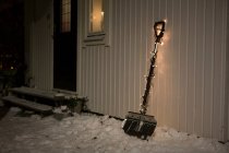 Pelle décorée avec des lumières de fées dans la neige près de la maison — Photo de stock