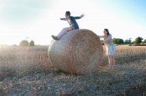 Молодые женщины играют на тюке сена в поле — стоковое фото