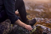 Abgeschnittenes Bild eines Mannes, der Schnürsenkel in den Bergen bindet — Stockfoto