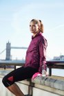 Femme en vêtements de sport assise à côté d'un pont — Photo de stock