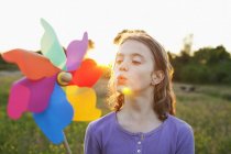 Girl blowing toy windmill at sunset — Stock Photo