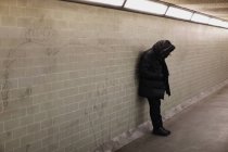 Человек в капюшоне, опирающийся на стену метро — стоковое фото