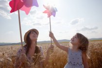 Mãe e filha no campo de trigo segurando moinho de vento — Fotografia de Stock
