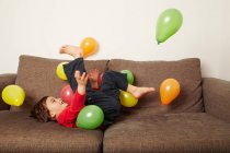 Giovane ragazzo sdraiato sul divano calci palloncini — Foto stock