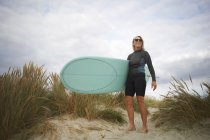 Портрет старшої жінки на піску, що тримає дошку для серфінгу — стокове фото