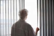 Вид ззаду на старшу жінку, яка дивиться з вікна — стокове фото