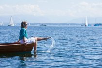 Jovem mulher sentada em um barco e salpicando água — Fotografia de Stock