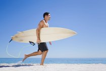 Uomo che trasporta tavola da surf sulla spiaggia — Foto stock