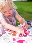 Little girl painting in a green field — Stock Photo