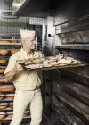 Glücklicher Bäcker legt Blech mit Scheibenbrot in den Ofen — Stockfoto