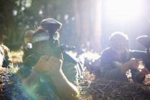 Paintball players lying on woods ground in sunlight in action — Stock Photo