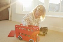 Девушка играет с игрушечным автобусом на полу — стоковое фото