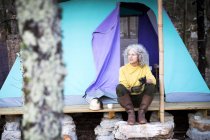 Mature woman sitting on woodland camping porch — Stock Photo