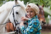 Smiling boy petting horse in yard, focus on foreground — Stock Photo