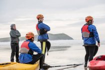 Quatre personnes sur la plage avec kayaks, Polzeath, Cornouailles, Angleterre — Photo de stock