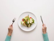 Mains tenant fourchette et couteau par salade — Photo de stock