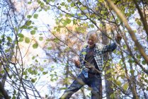 Junge im Grundschulalter klettert im Herbstpark auf Baum — Stockfoto