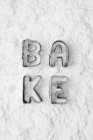 Cookie cutters spelling bake in flour — Stock Photo