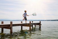 Boy running on dock with fishing net — Stock Photo