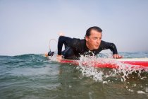 Человек лежит на доске для серфинга в воде — стоковое фото