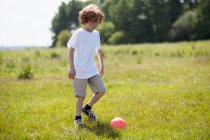 Хлопчик штовхає футбольний м'яч у полі — стокове фото
