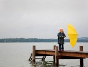 Girl holding yellow umbrella on dock — Stock Photo