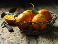Oranges in basket with one halved on rustic wooden table — Stock Photo