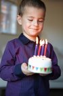 Niño sosteniendo pastel en miniatura con velas - foto de stock