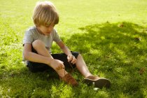 Хлопчик зв'язує черевик у траві — стокове фото